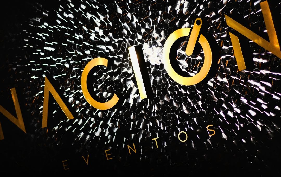 Detalle del logo NACIÓN dorado sobre la pared de mosaico